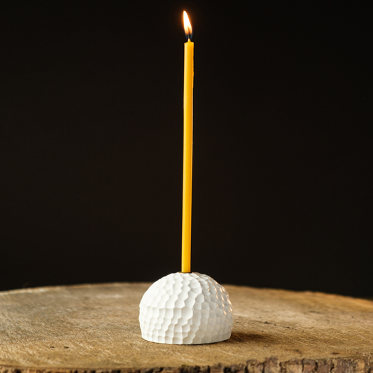 White textured candle holder with a yellow candle on a wooden surface and black background