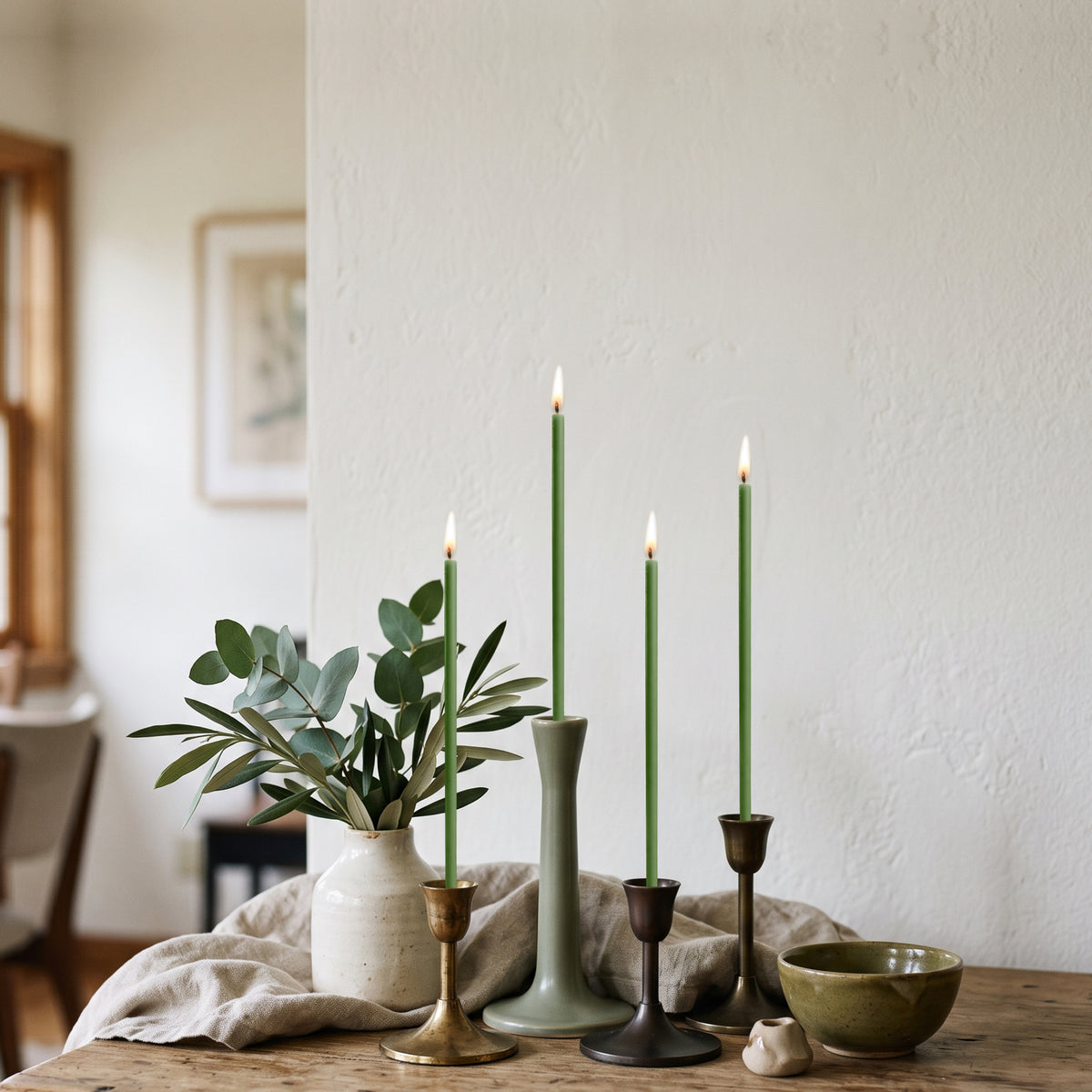 Green beeswax taper candles 6.3″, lit in brass candlesticks