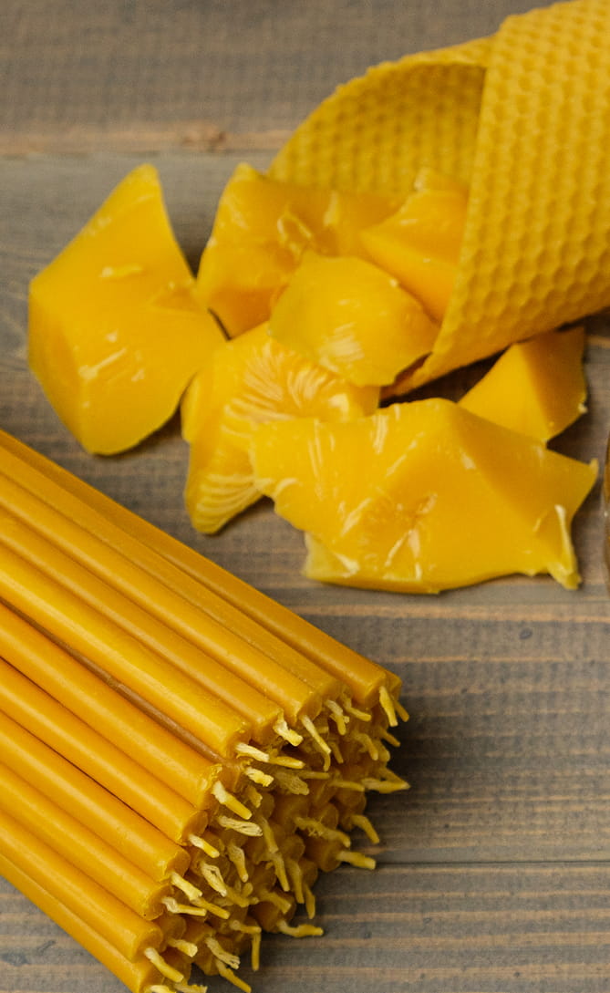 Rolled honeycomb beeswax sheet and chunks of raw beeswax next to hand-dipped taper candles with cotton wicks on weathered wood