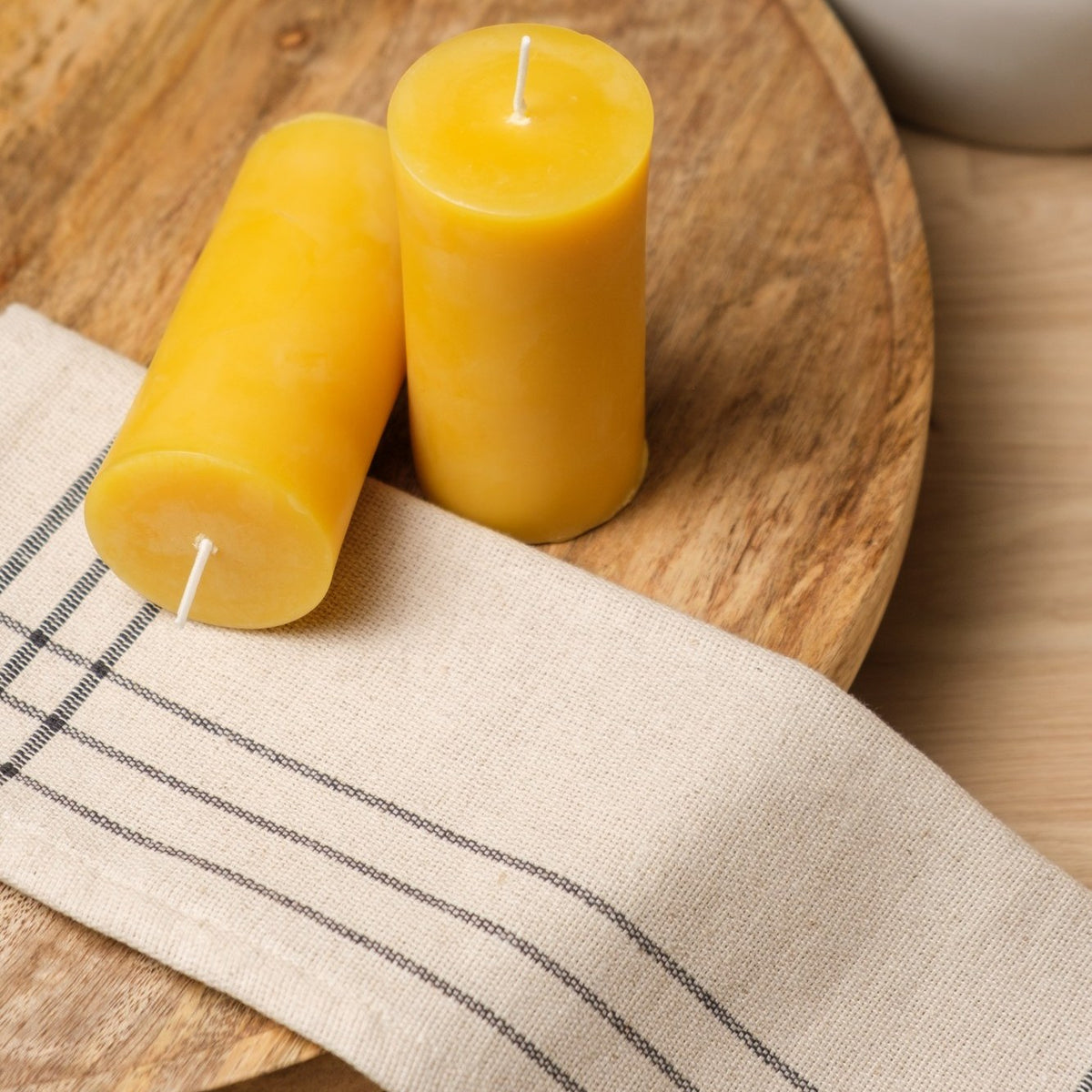 Natural beeswax pillar candles 2 by 4 inch, two candles on a wooden board with linen