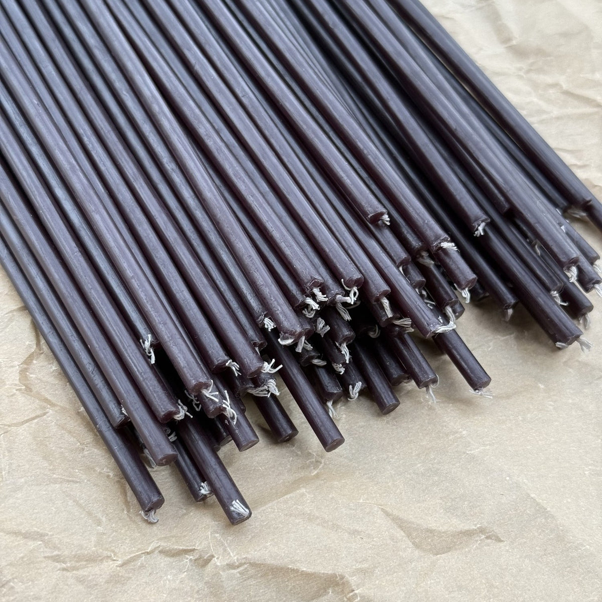 Black beeswax taper candles 6.3″, loose tapers closeup on kraft paper