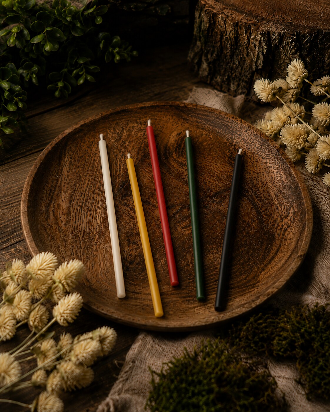 Five colors of Closterra beeswax tapers on a wooden plate