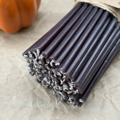 Black beeswax taper candles 6.3″, bundle of 100 with wick ends beside a pumpkin