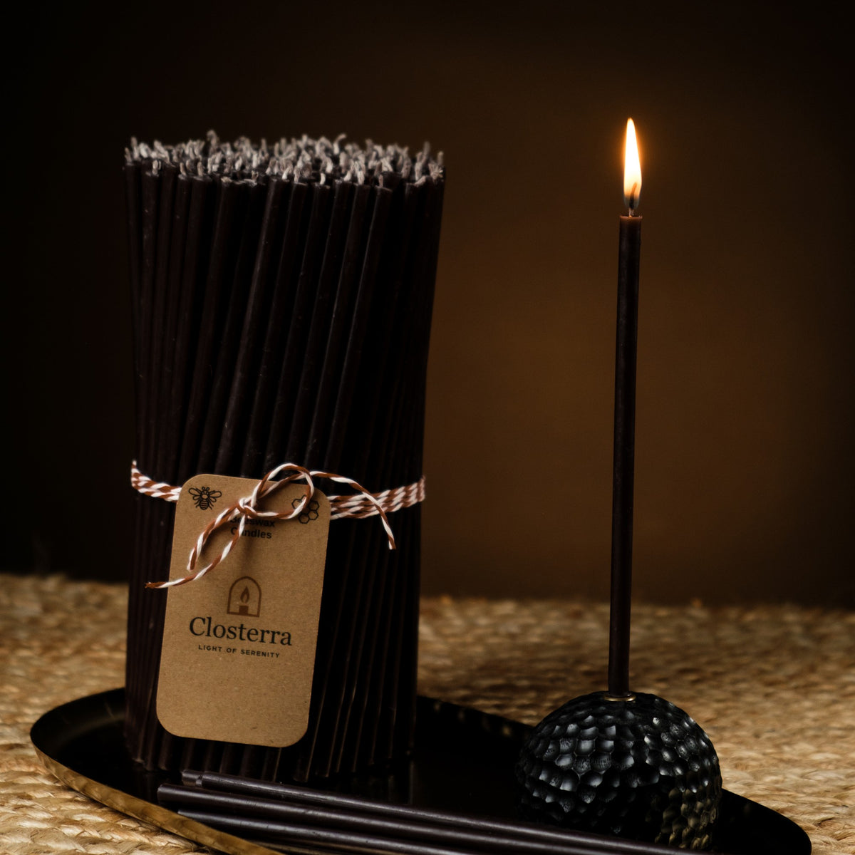 Black beeswax taper candles 7.3″, lit taper in a black holder beside a bundle with a Closterra tag