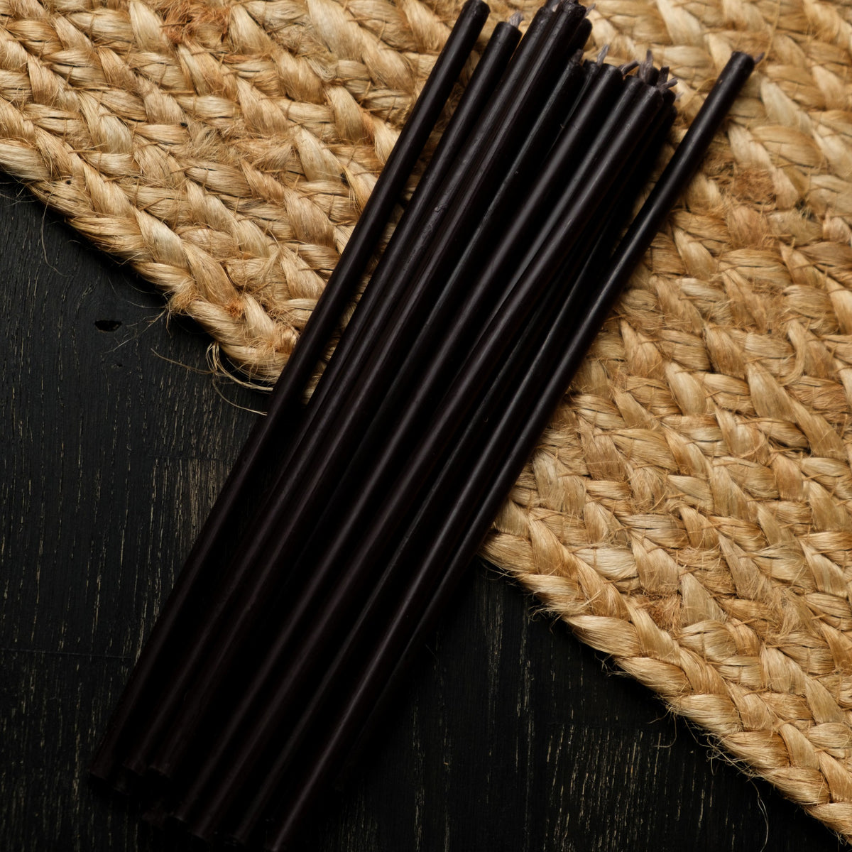Black beeswax taper candles 7.3″, loose tapers on dark wood and a jute mat