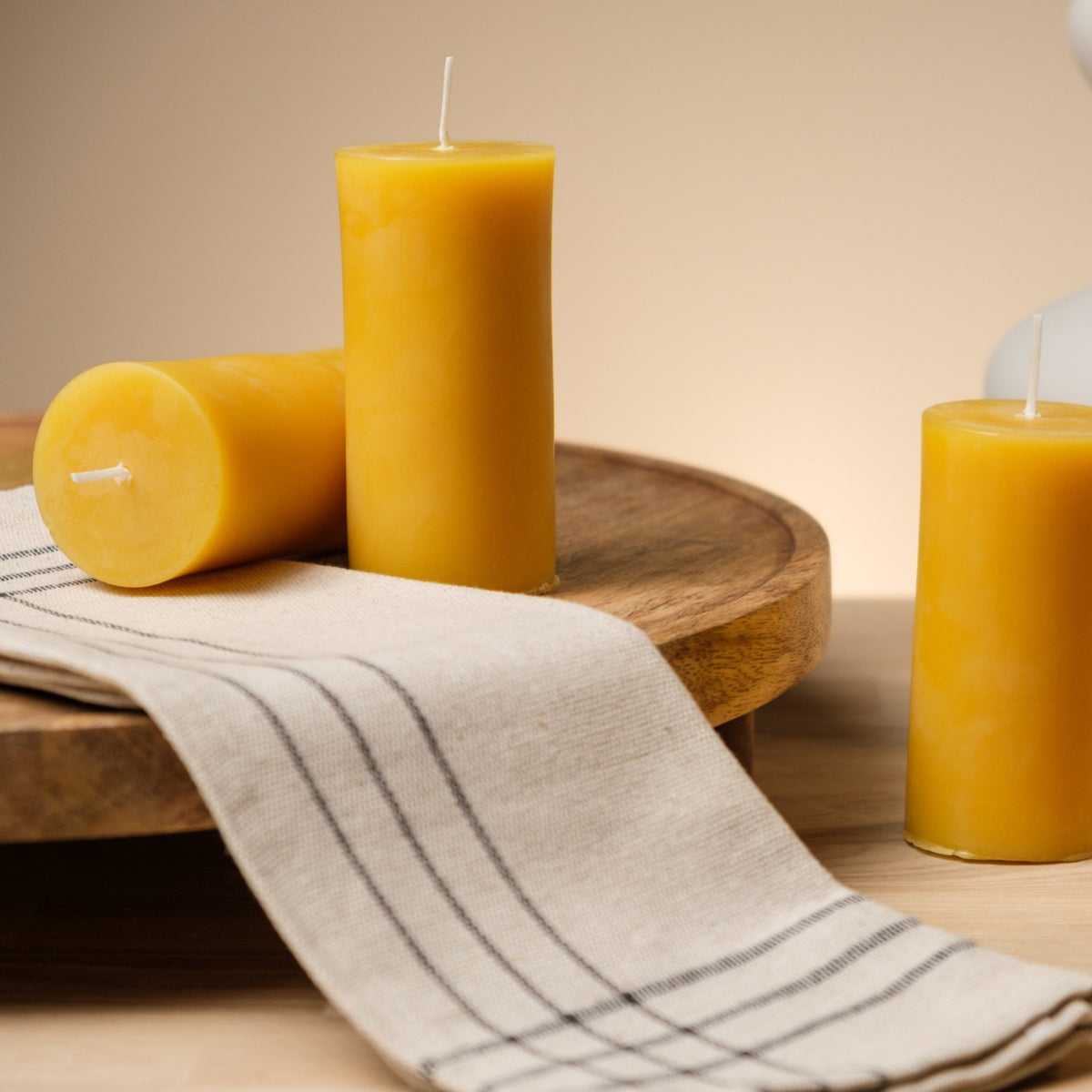 Natural beeswax pillar candles 2 by 4 inch, three candles on a wooden board with striped linen