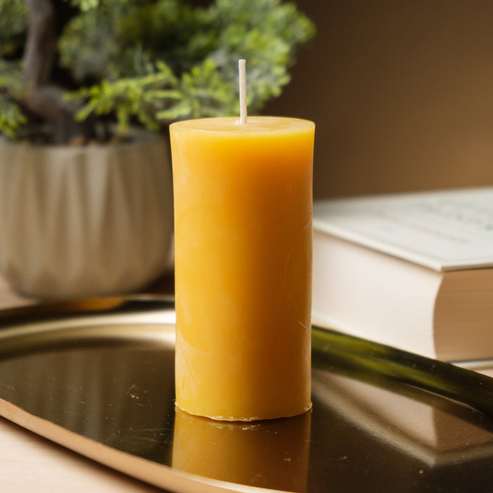 Natural beeswax pillar candle, 2 by 4 inch and undyed, on a brass tray