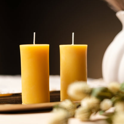 Close-up of two natural beeswax pillar candles showing the golden undyed wax and cotton wick