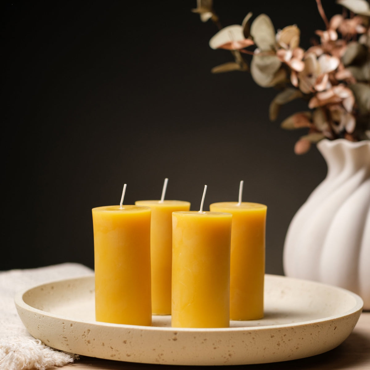 Lit natural beeswax pillar candle on a plate with eucalyptus