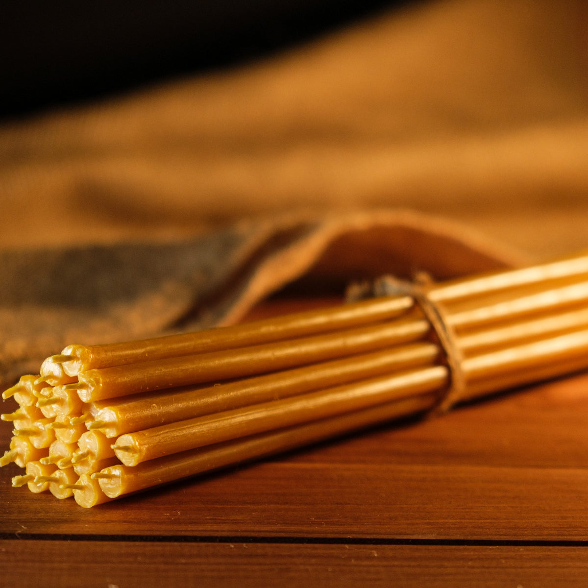 Natural yellow beeswax taper candles 6.5″, bundle tied with twine on wood, close-up of the wicks