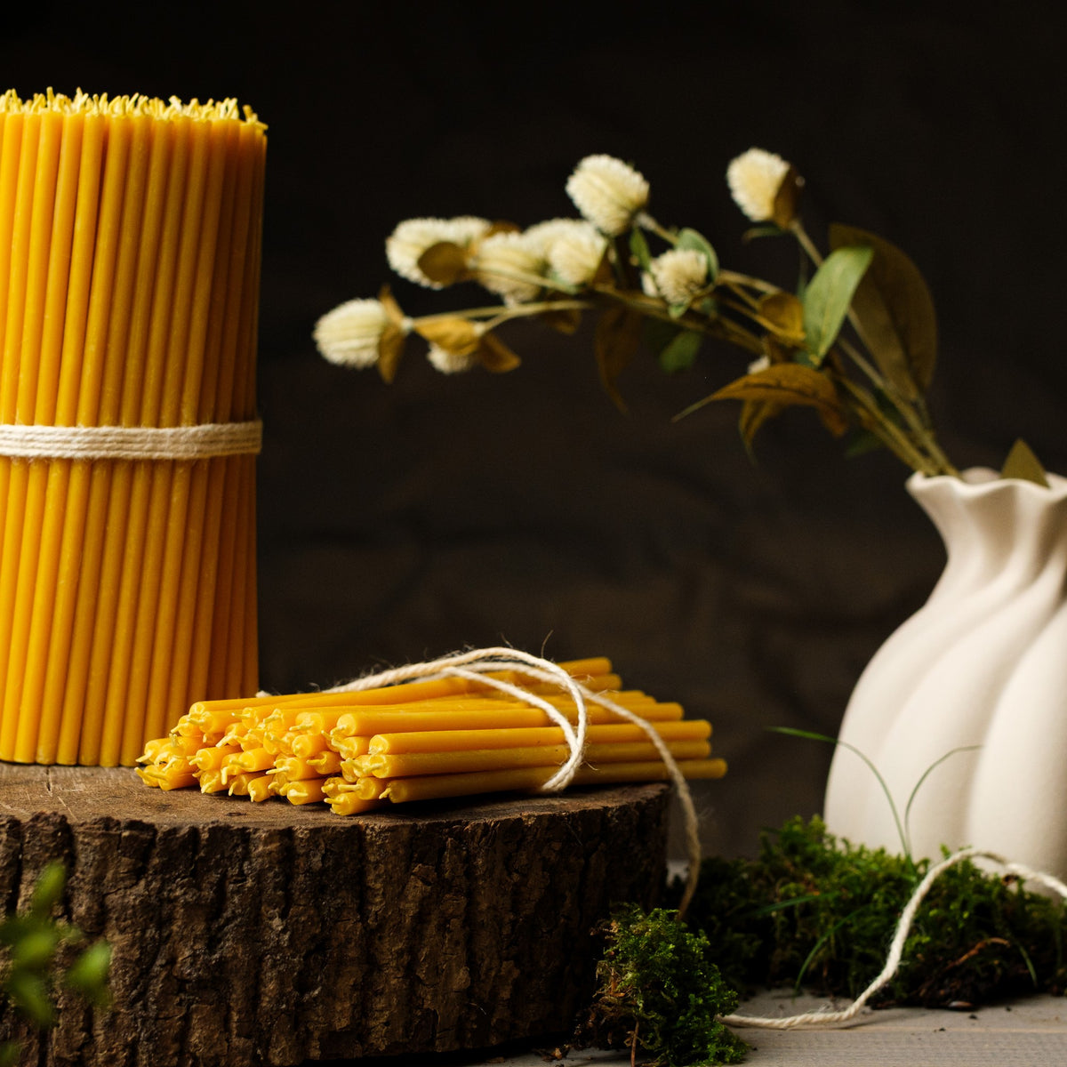 Natural yellow beeswax taper candles 7.3″, bundles on a wood stump with dried flowers