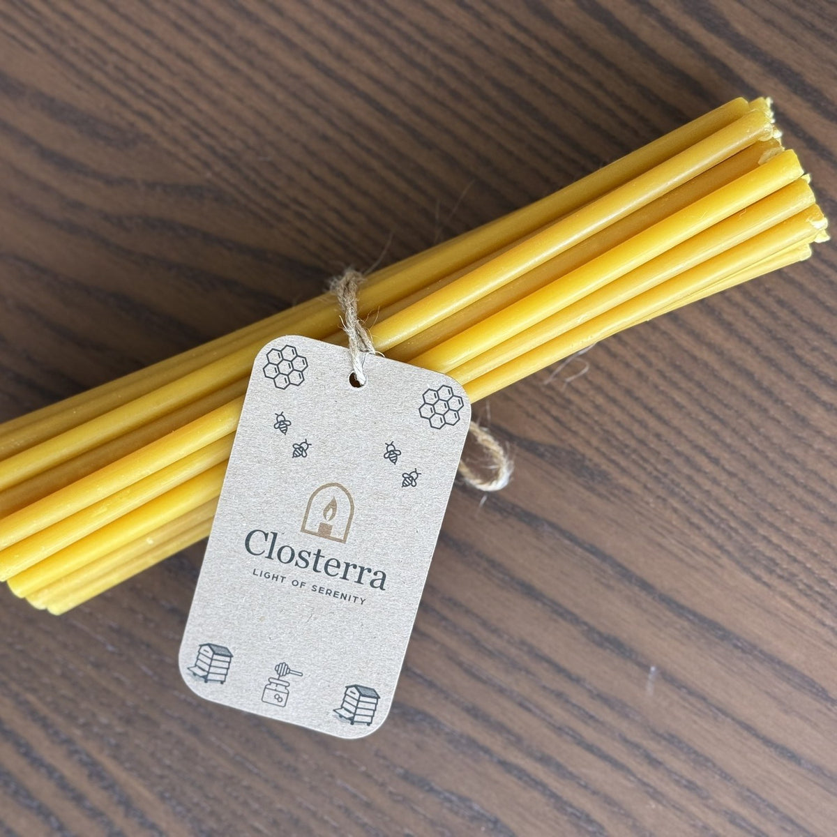 Natural yellow beeswax taper candles 8″, bundle of 25 with Closterra tag on wood