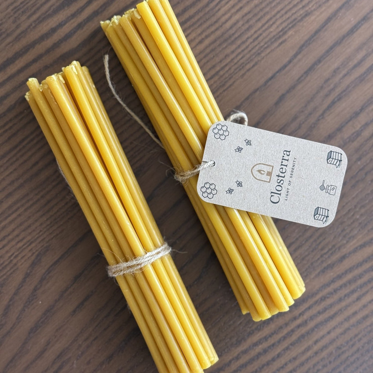 Natural yellow beeswax taper candles 8″, bundles of 20 and 25 side by side on wood