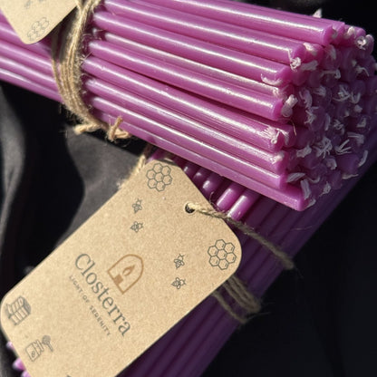 Purple beeswax taper candles, tagged bundles closeup on black satin