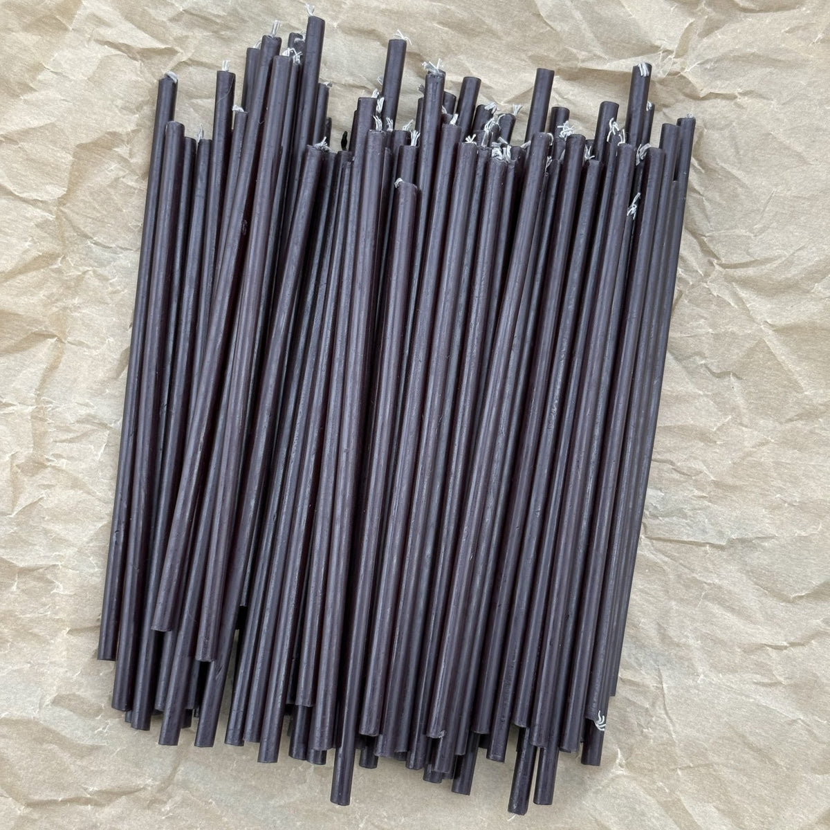 Loose thin black beeswax ritual candles on crinkled kraft paper