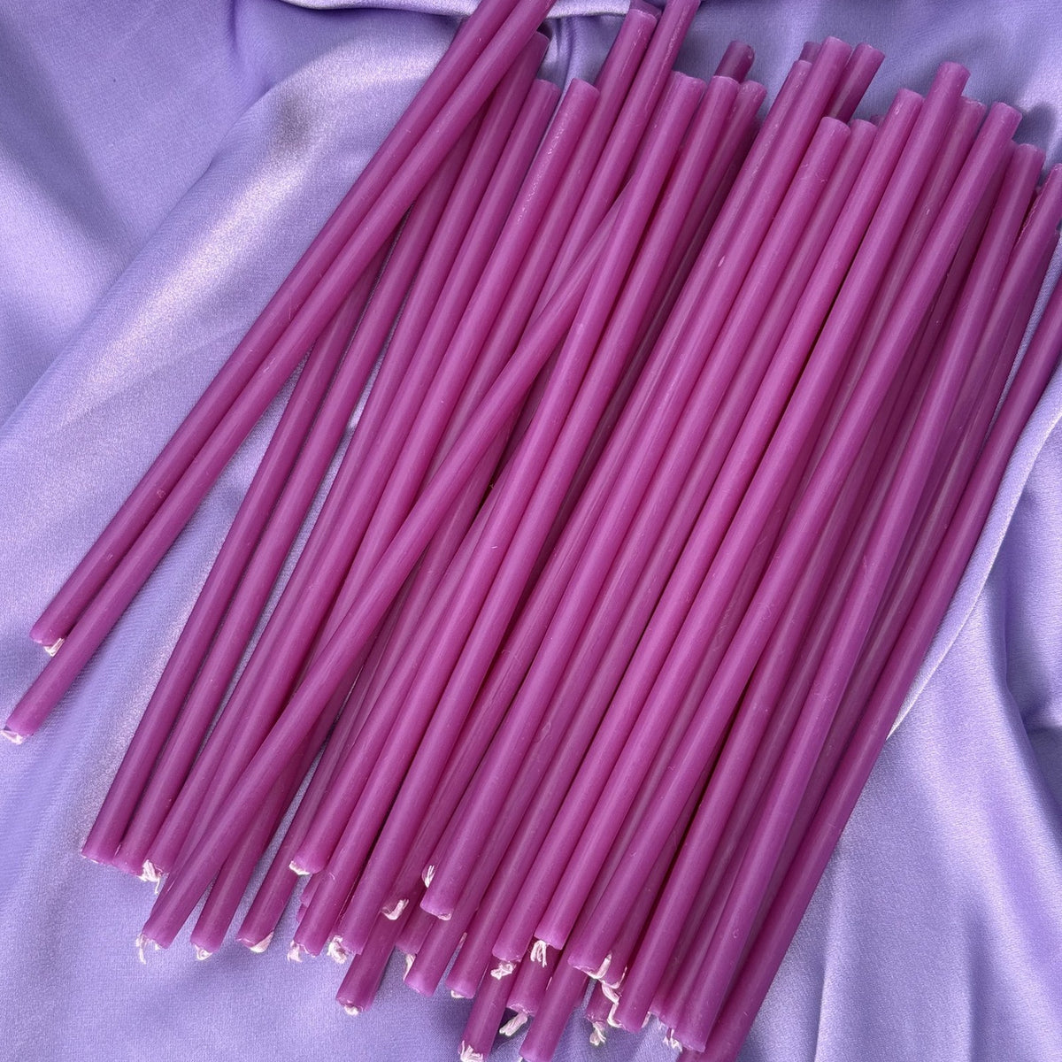 Loose thin purple beeswax ritual candles on lilac satin