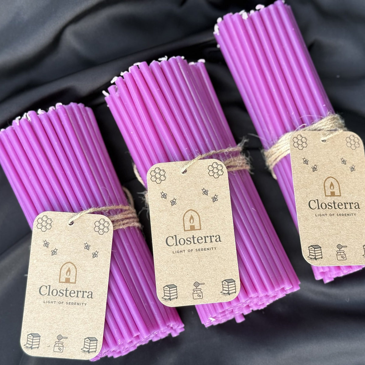 Three bundles of purple beeswax ritual candles with Closterra tags on black satin