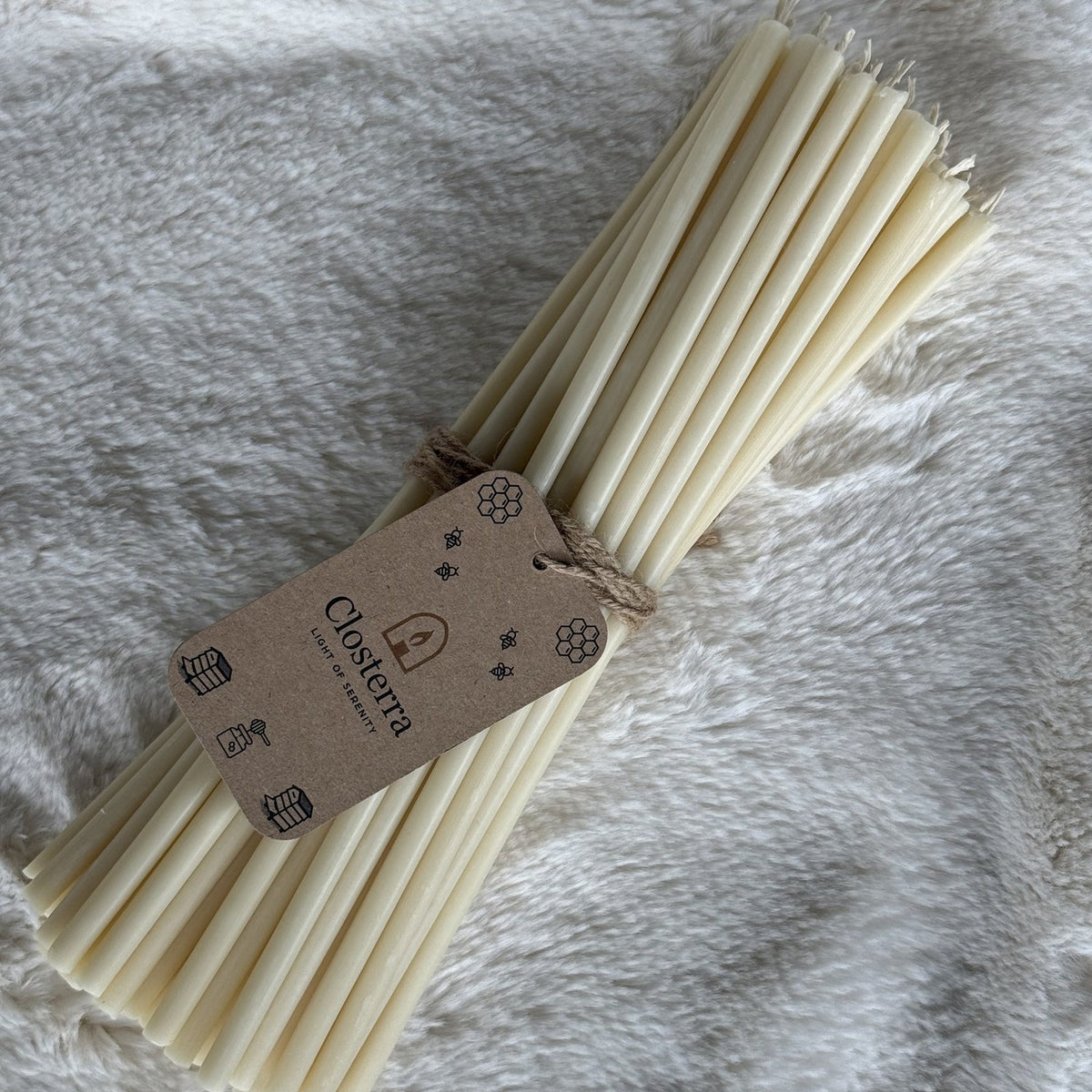Bundle of white beeswax ritual candles with a Closterra tag on white faux fur