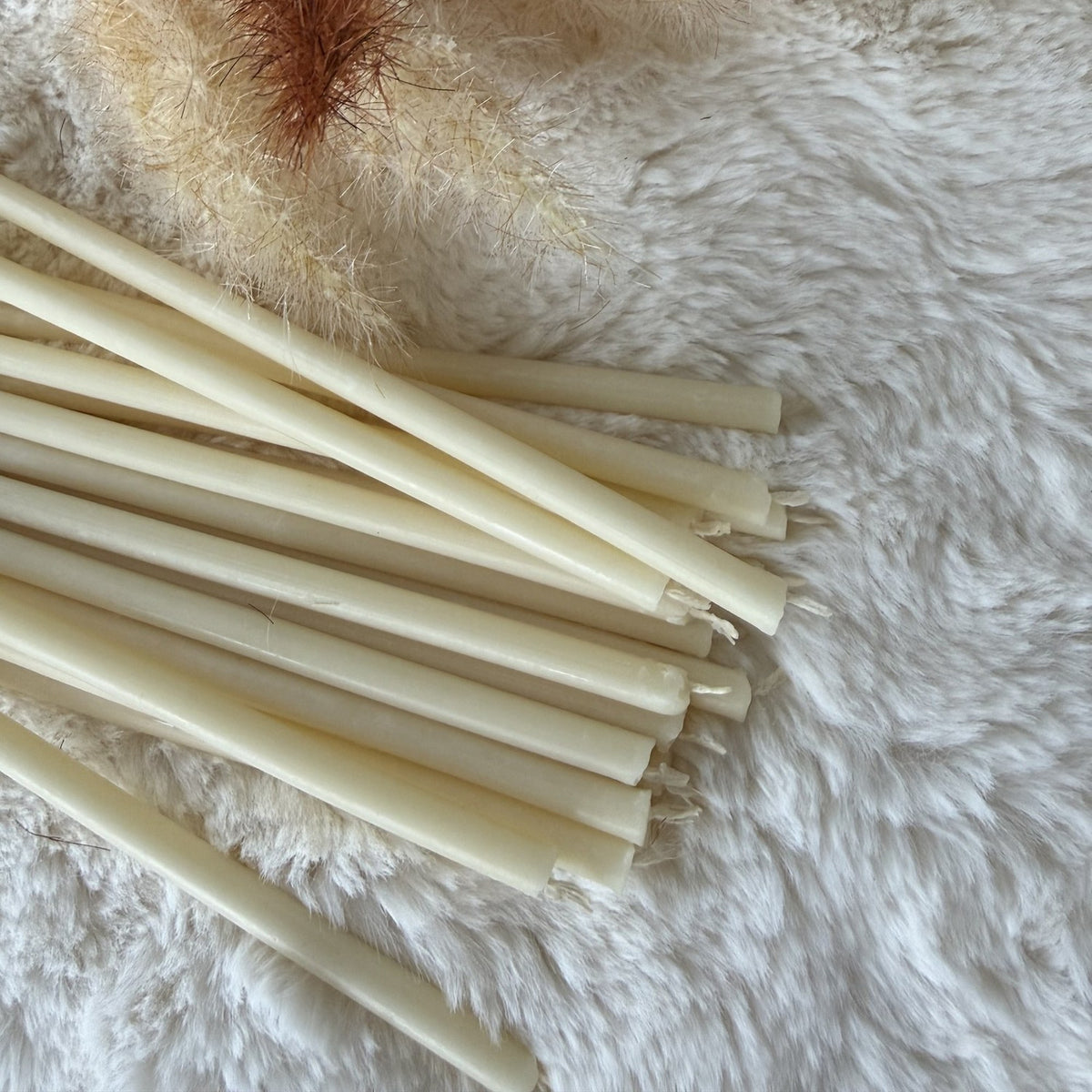White beeswax ritual candles on white faux fur with pampas grass