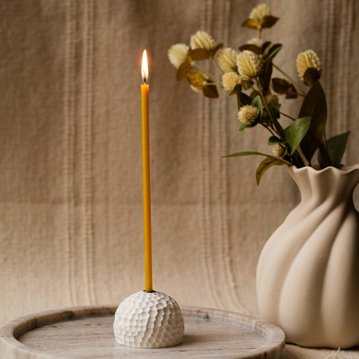 Closterra thin natural yellow beeswax taper candles, lit in a vase