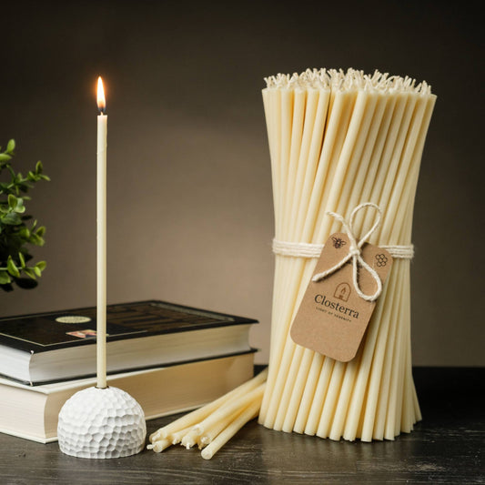 Closterra thin white beeswax taper candles, lit, with a Closterra gift tag