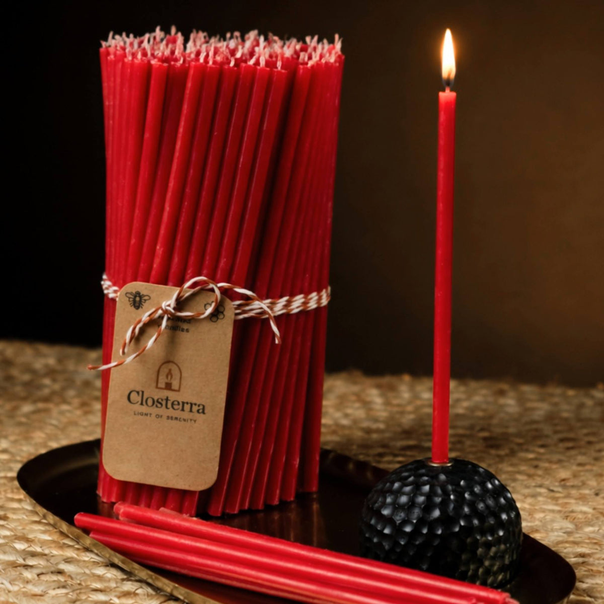 Closterra thin red beeswax taper candles, lit, with a Closterra gift tag