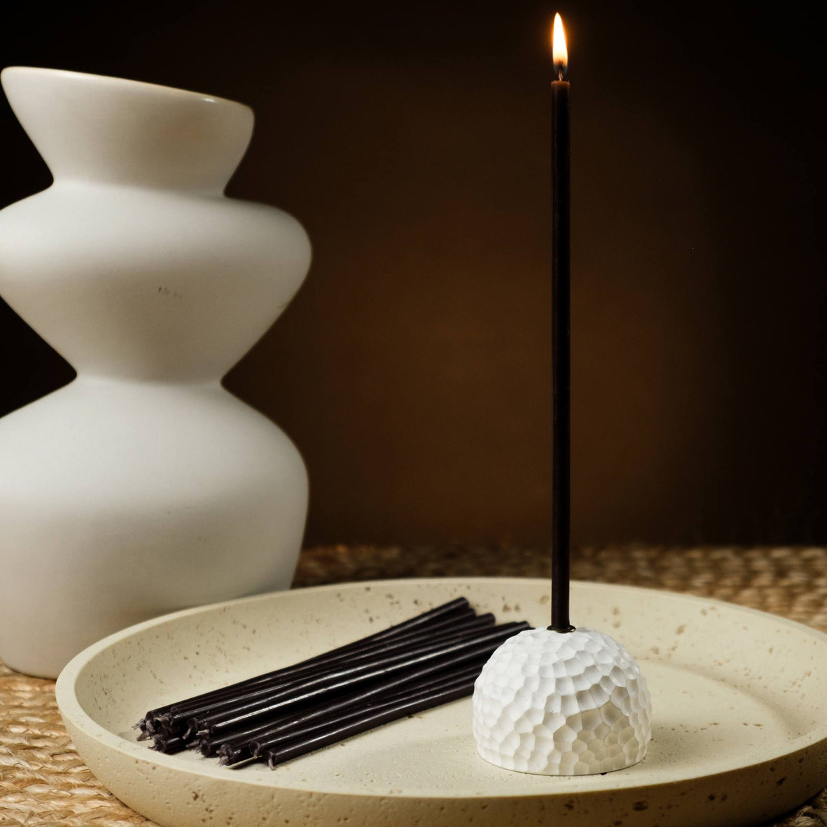 Closterra thin black beeswax taper candles, lit in a candle holder