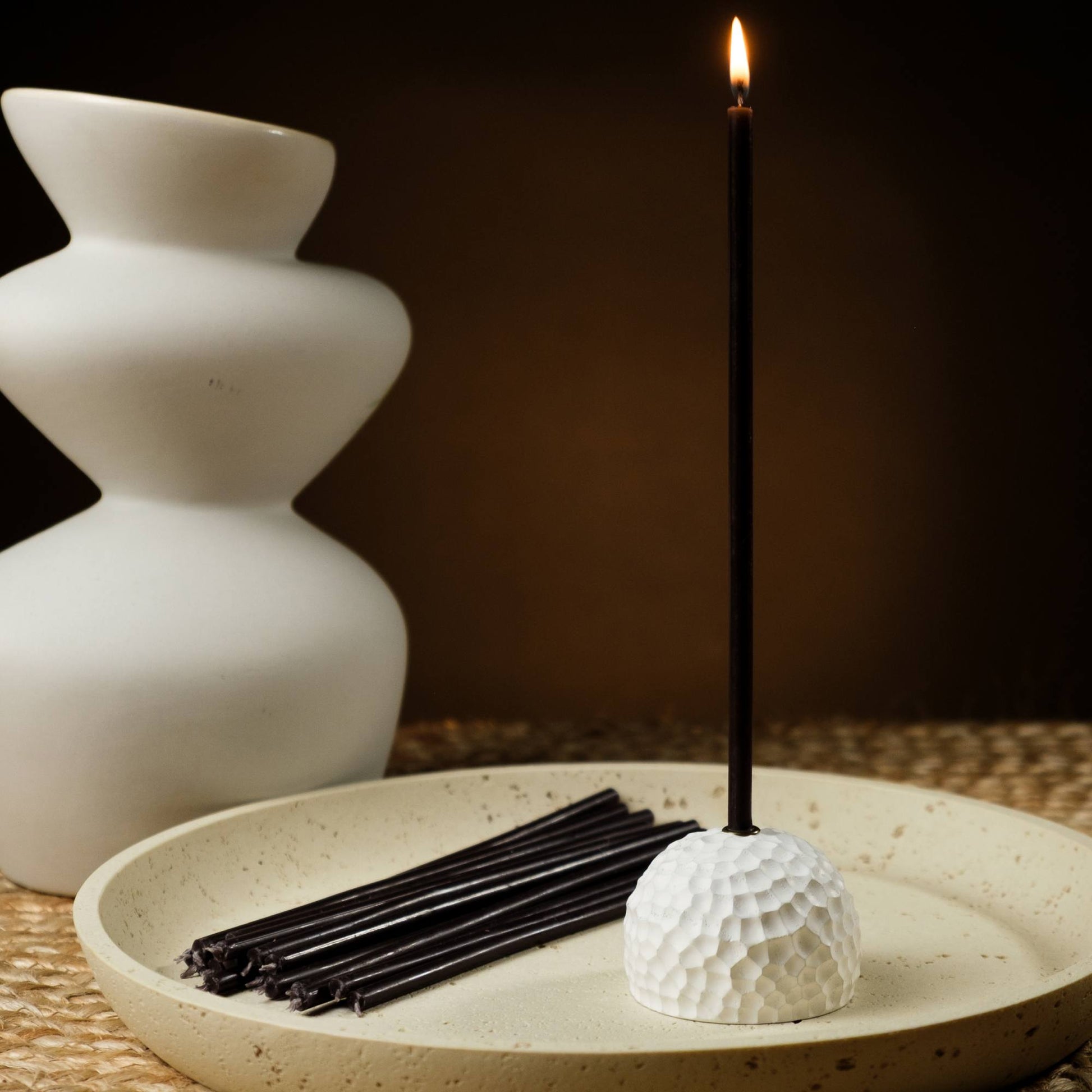 Closterra thin black beeswax taper candles, lit in a candle holder
