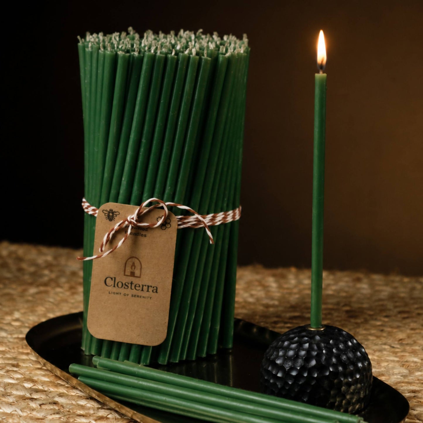 Closterra thin green beeswax taper candles, lit, with a Closterra gift tag