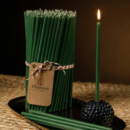 Closterra thin green beeswax taper candles, lit, with a Closterra gift tag
