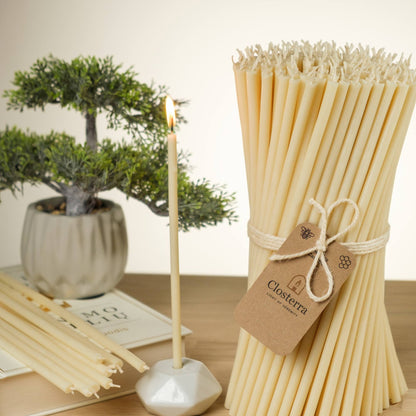 Closterra thin white beeswax taper candles, lit in a candle holder