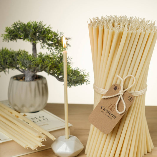 Closterra thin white beeswax taper candles, lit in a candle holder