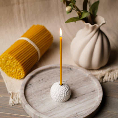 Closterra thin natural yellow beeswax taper candles, lit in a candle holder