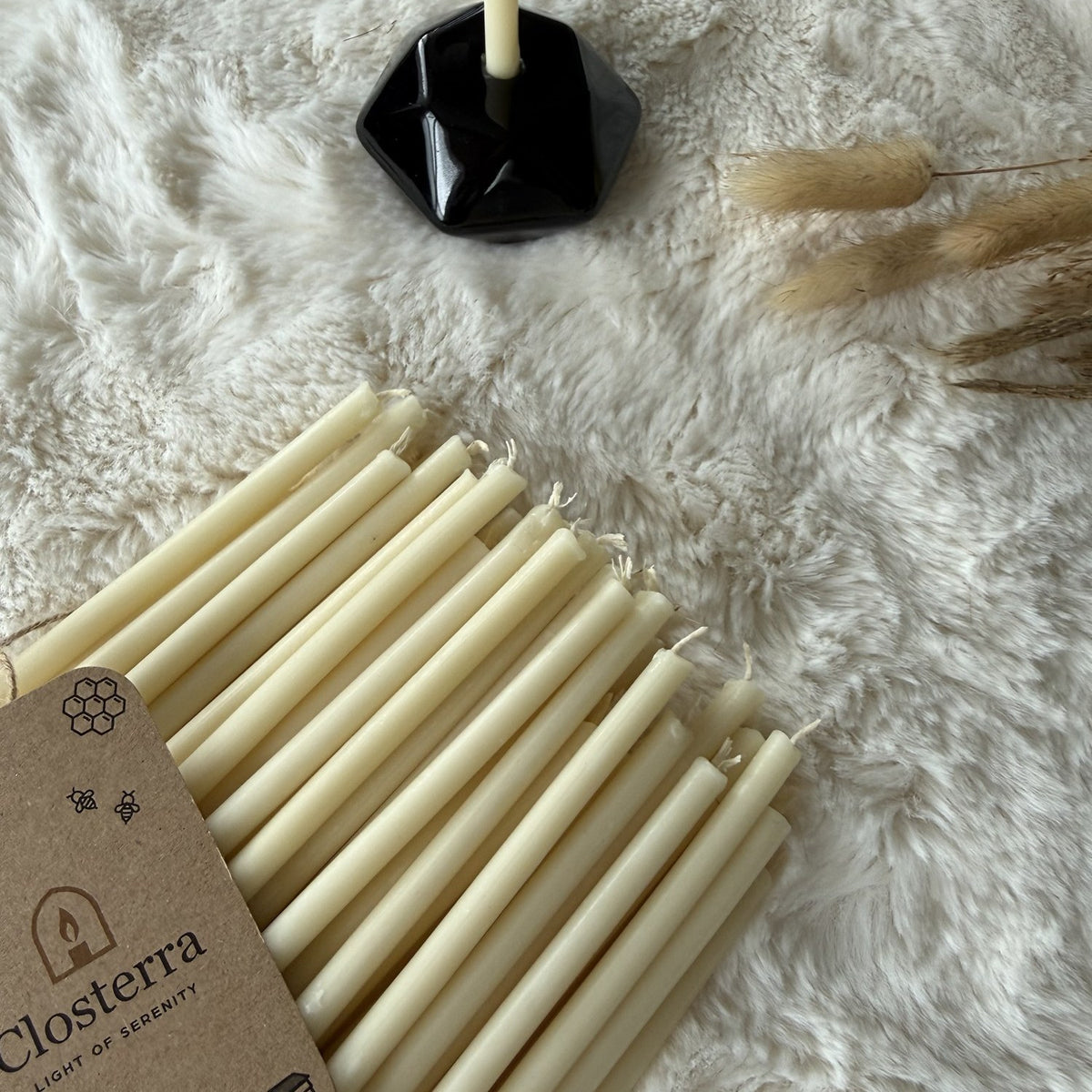 White beeswax taper candles 10.4″, tapers with Closterra tag and a black holder on white fur