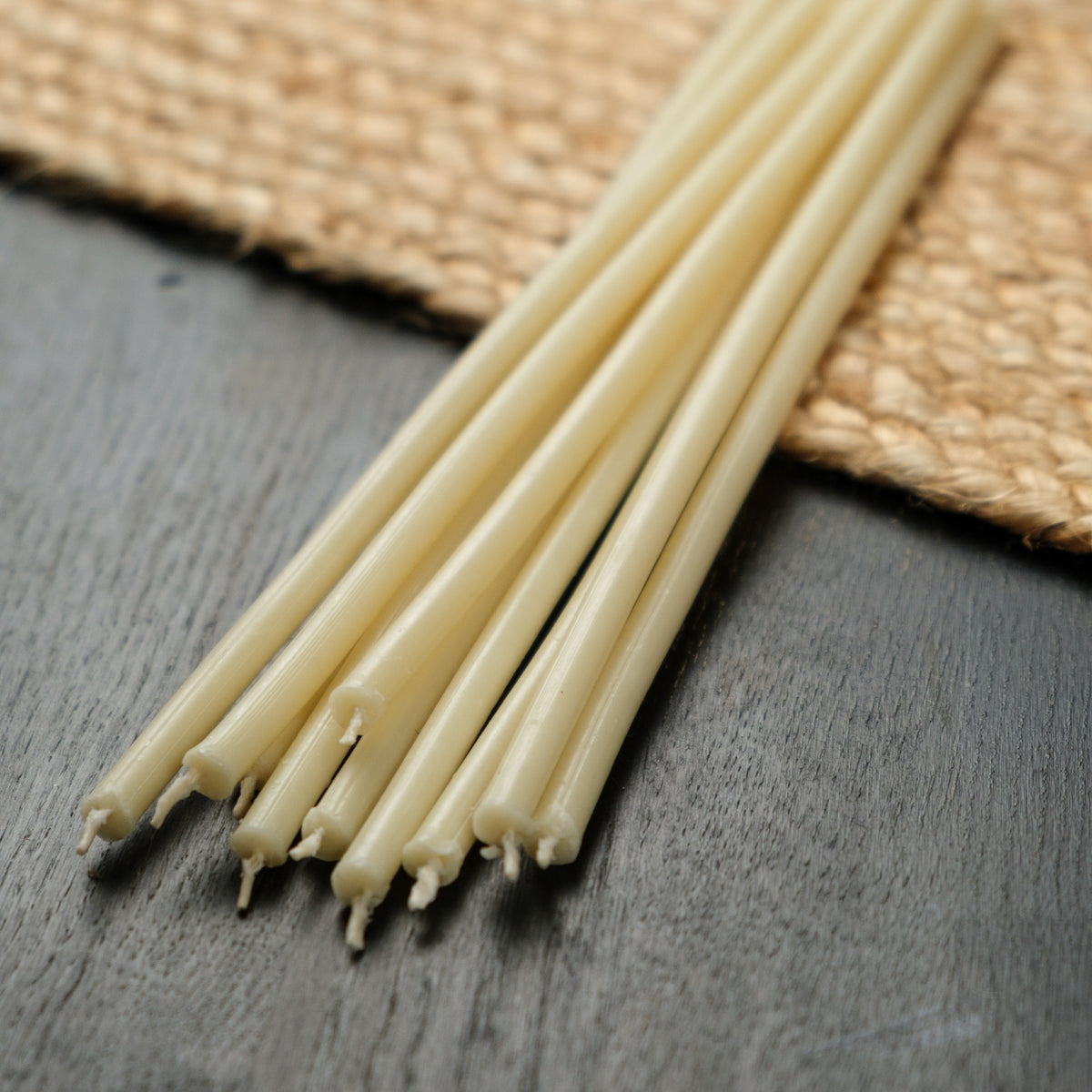 White beeswax taper candles 6.3″, loose tapers on dark wood and a jute mat