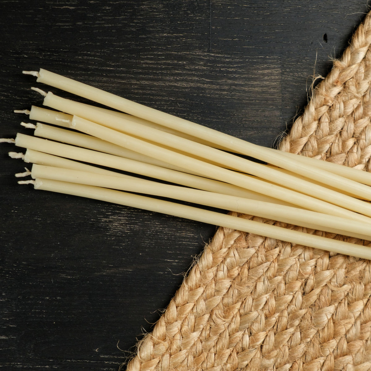 White beeswax taper candles 6.5″, loose tapers on dark wood and a jute mat