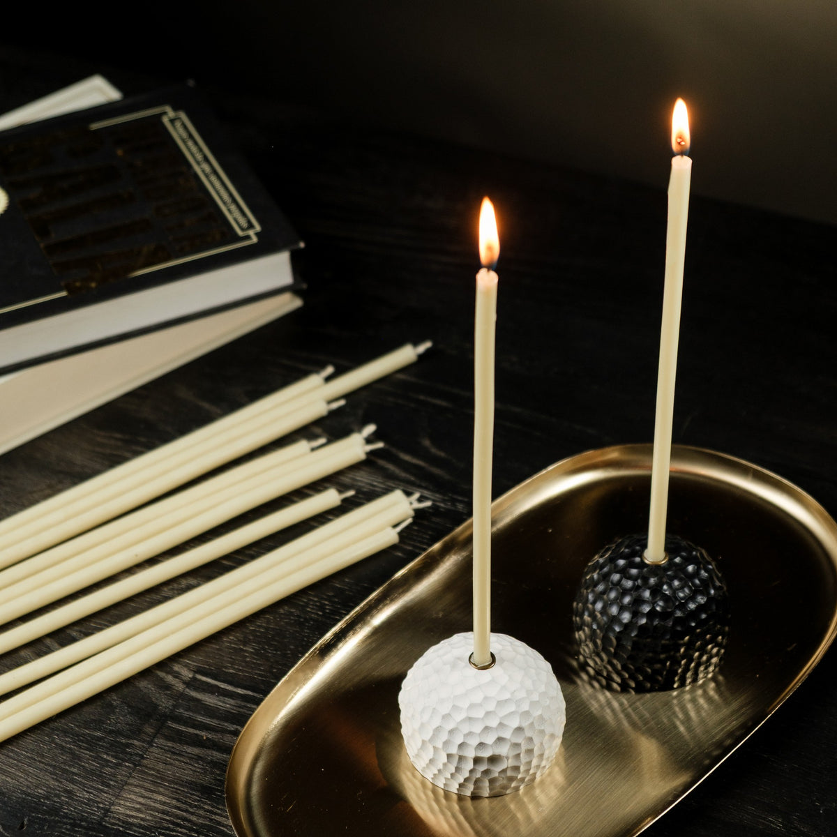 White beeswax taper candles 7.3″, two lit tapers in white and black holders on a gold tray