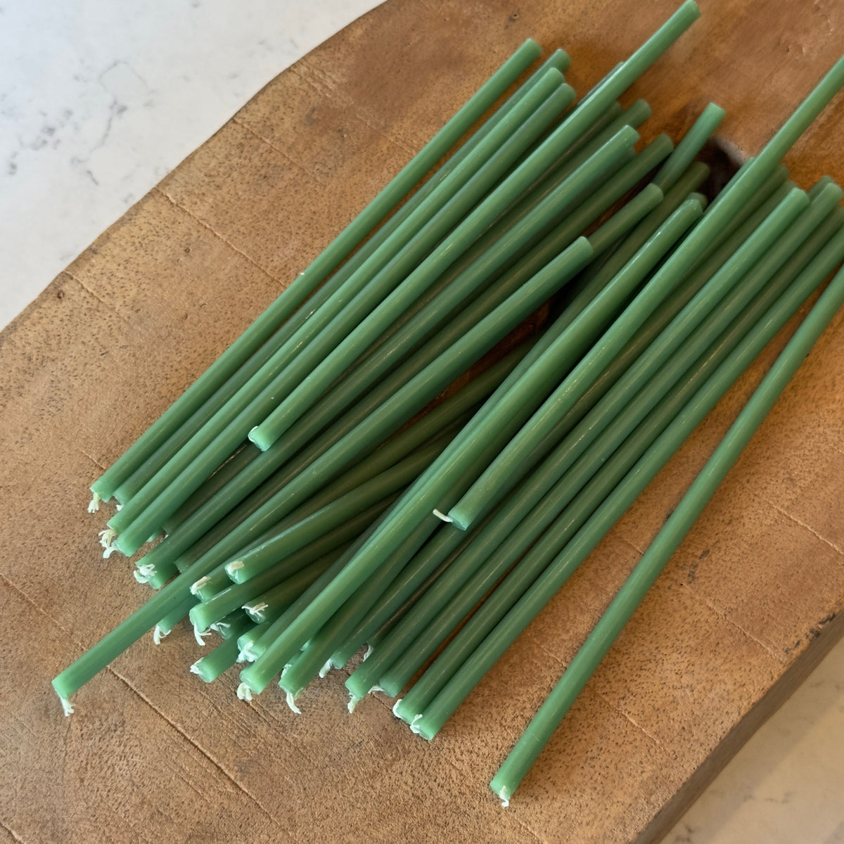 Green beeswax taper candles 6.3″, scattered on cutting board