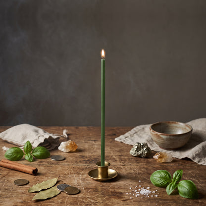 Green thin beeswax ritual candle for Money & Abundance, 8 inch, lit in a brass holder with coins, basil, bay leaves, pyrite and citrine, Closterra