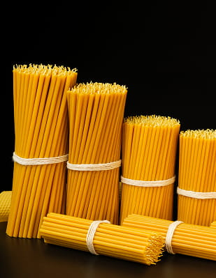 Bundles of pure beeswax taper candles in graduated sizes tied with string on a dark surface